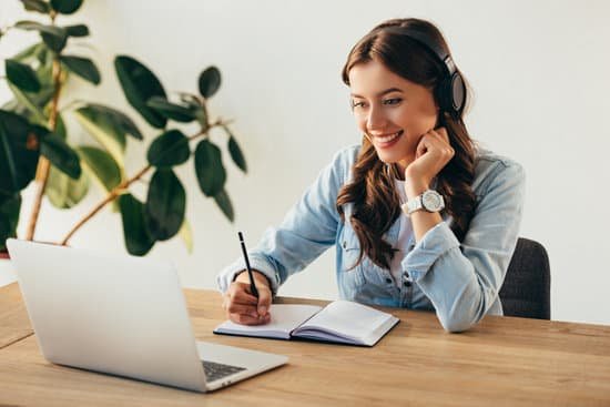 Women looking at computer with headphones on, writing in a journal. 